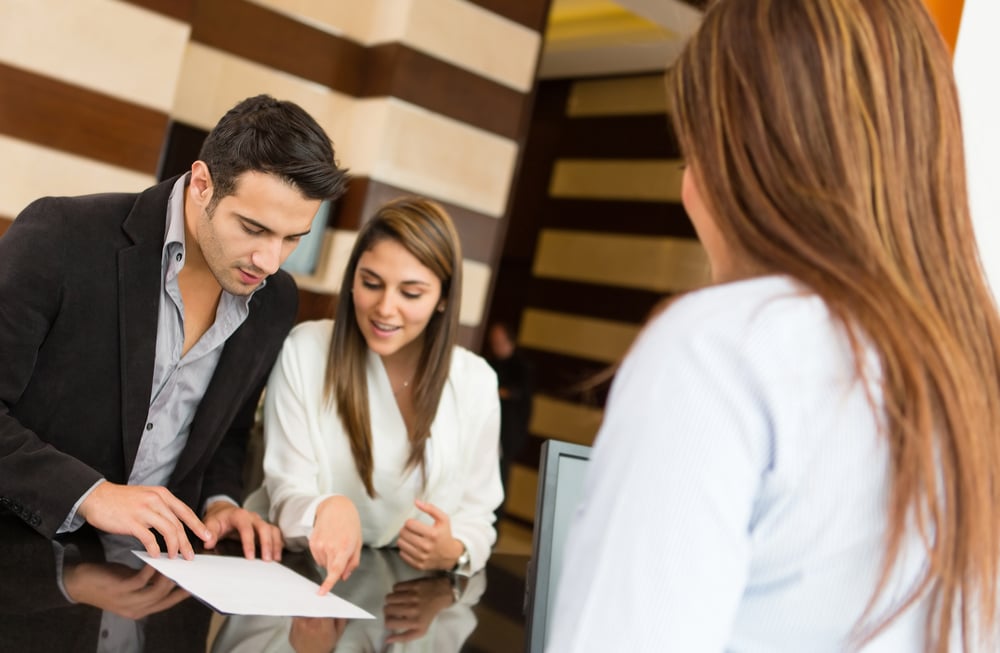 Hotel patrons reviewing terms and speaking to front desk team.