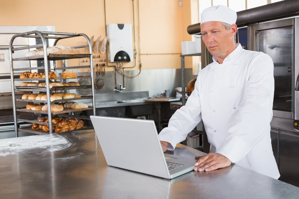 Restaurant owner looks at laptop, planning shifts for the upcoming week.
